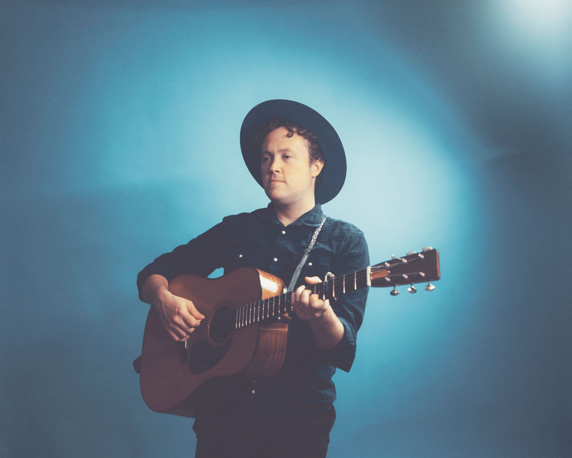 A man with a hat holds an acoustic guitar, showcasing his musical talent.