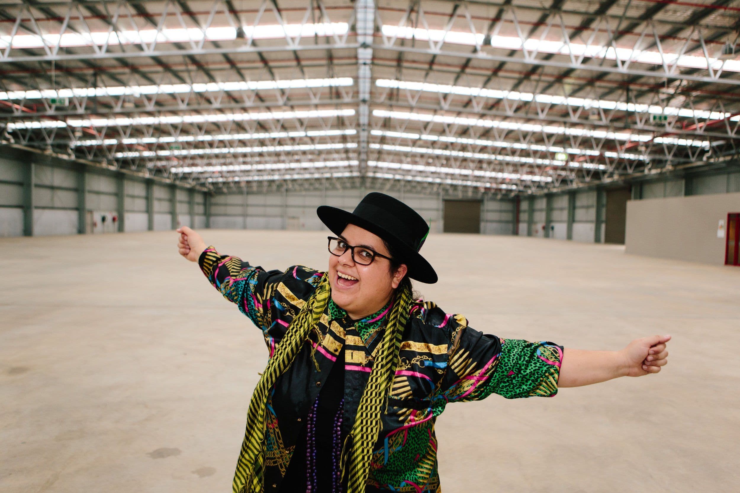 A person wearing a hat and coat stands alone in a spacious, empty warehouse.